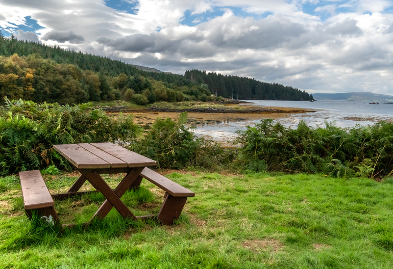 A picnic bench overlooking the shoreline and sea with islands in the background