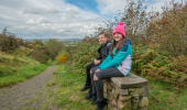 A boy and girl sitting on a stone bench next to a countryside footpath