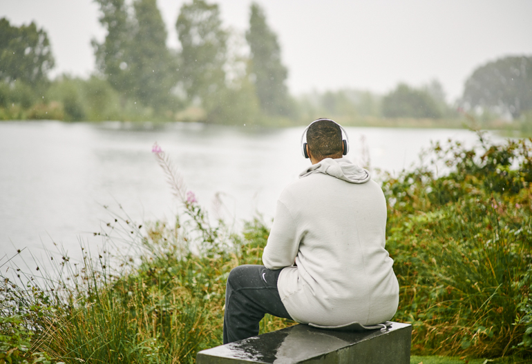 A man sits on a bench looking out towards a pond