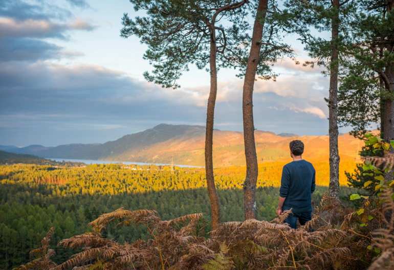 Rear view of man at Torr Dhuin looking across panorama as evening sun spills across River Oich and surrounding mountain range, near Fort Augustus