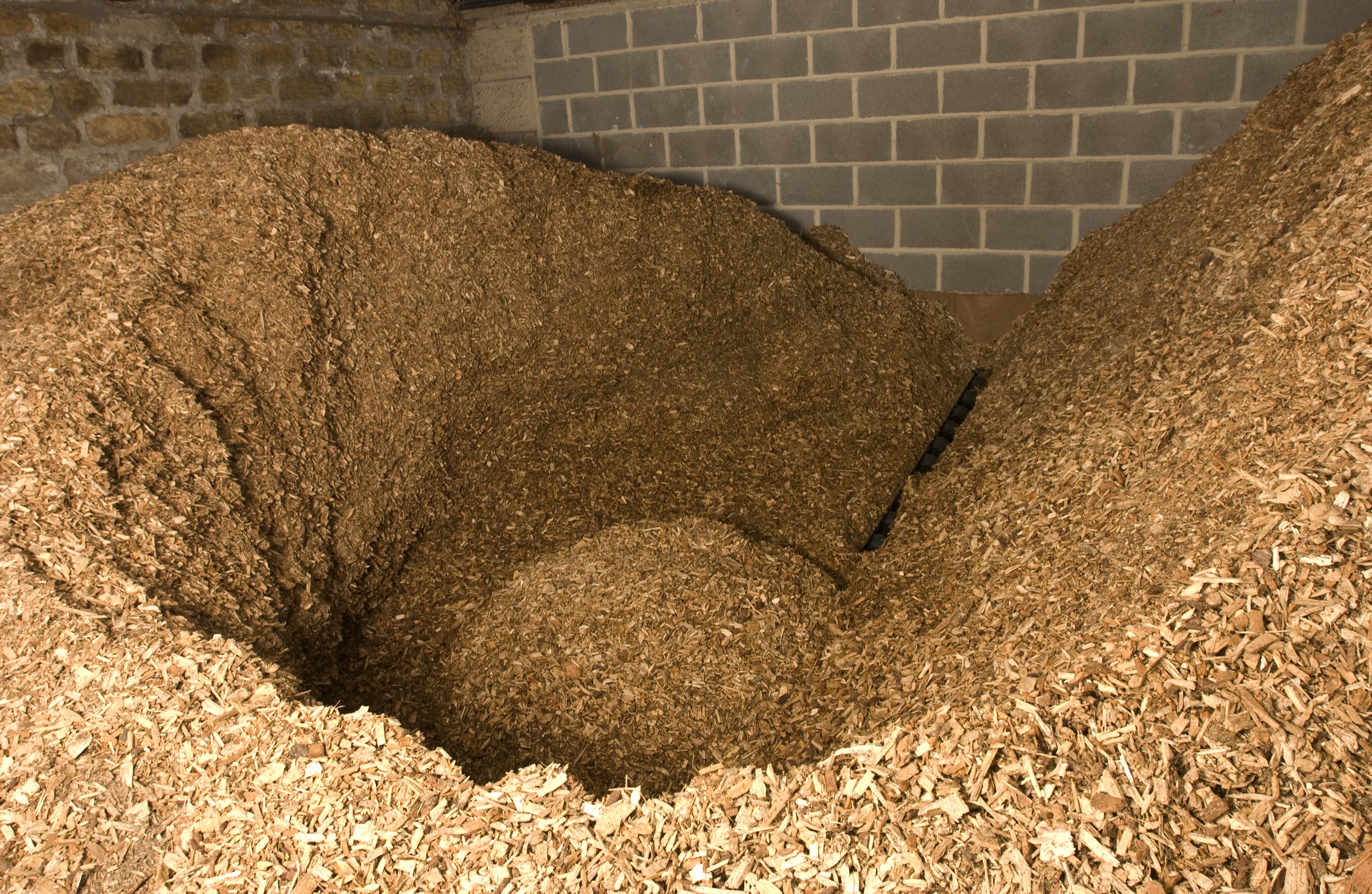 A large collection of wood chips mounded in a room with exposed brick walls. 
