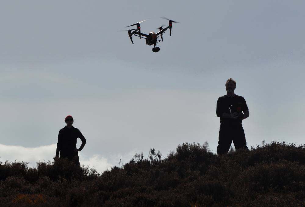 Silhouette of two people on a hillside with a drone hovering above