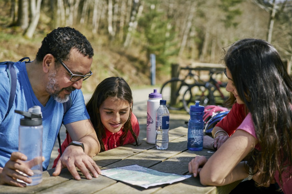 A family sitting at a picnic table studying a map