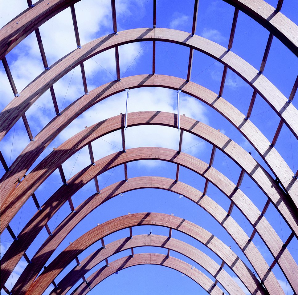 Uncompleted building showing a laminated timber frame with extremely curved roof under a blue sky