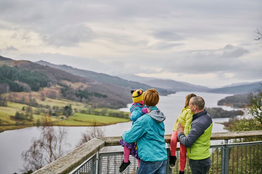 a family of four standing at a lookout over a loch