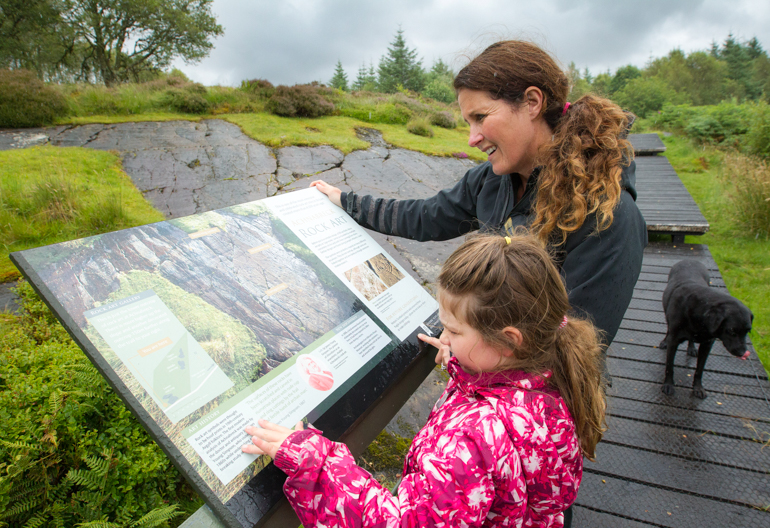 A woman and child read an information board in a forest