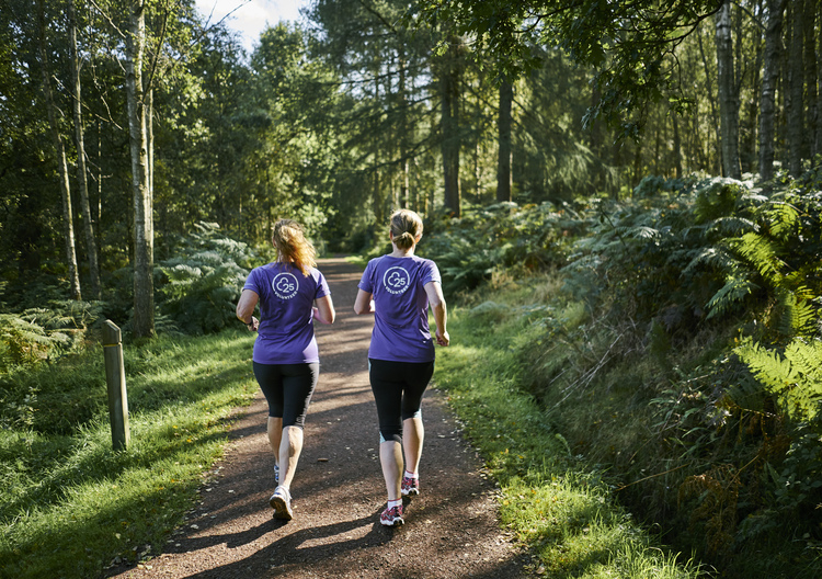 Rear view of two female runners running on tree lined track in Callendar Park parkrun, Falkirk