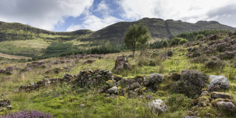 Rocks and heather covering the site of a ruined Highland Clearance village of Aoineadh Mor, with hills in the background