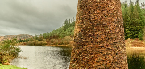 A brick structure next to a loch with trees along the bank