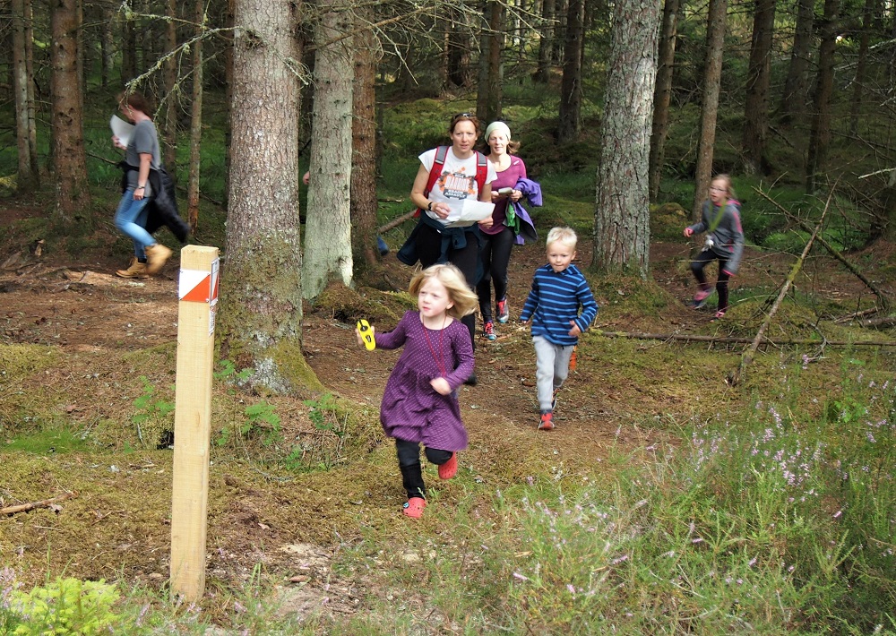 Two women follow a young girl and boy towards an orienteering marker post 