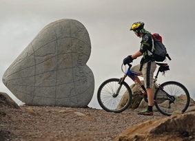 Mountain biker resting next to a large heart-shaped carved stone
