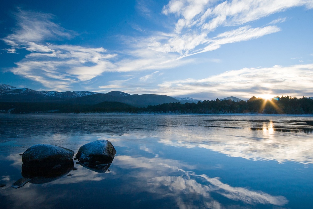 Landscape view of calm loch with two large boulders and blue sky