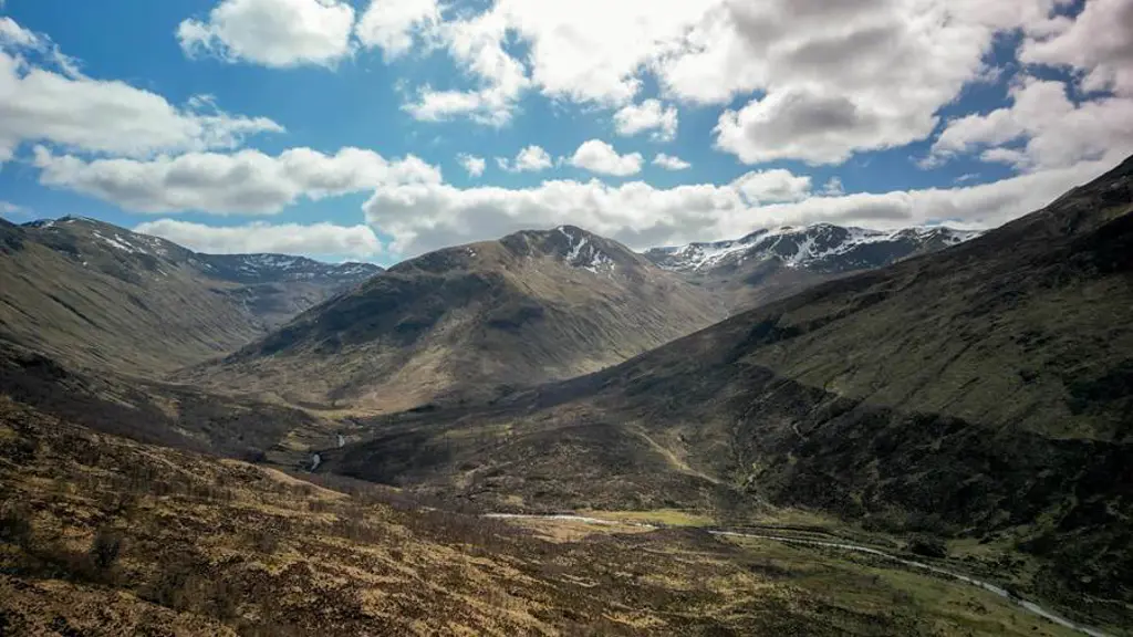 Snow-capped mountains stand against blue skies with white clouds. 
