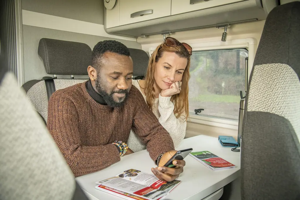 couple sitting at table inside campervan looking at maps, leaflets and mobile phones