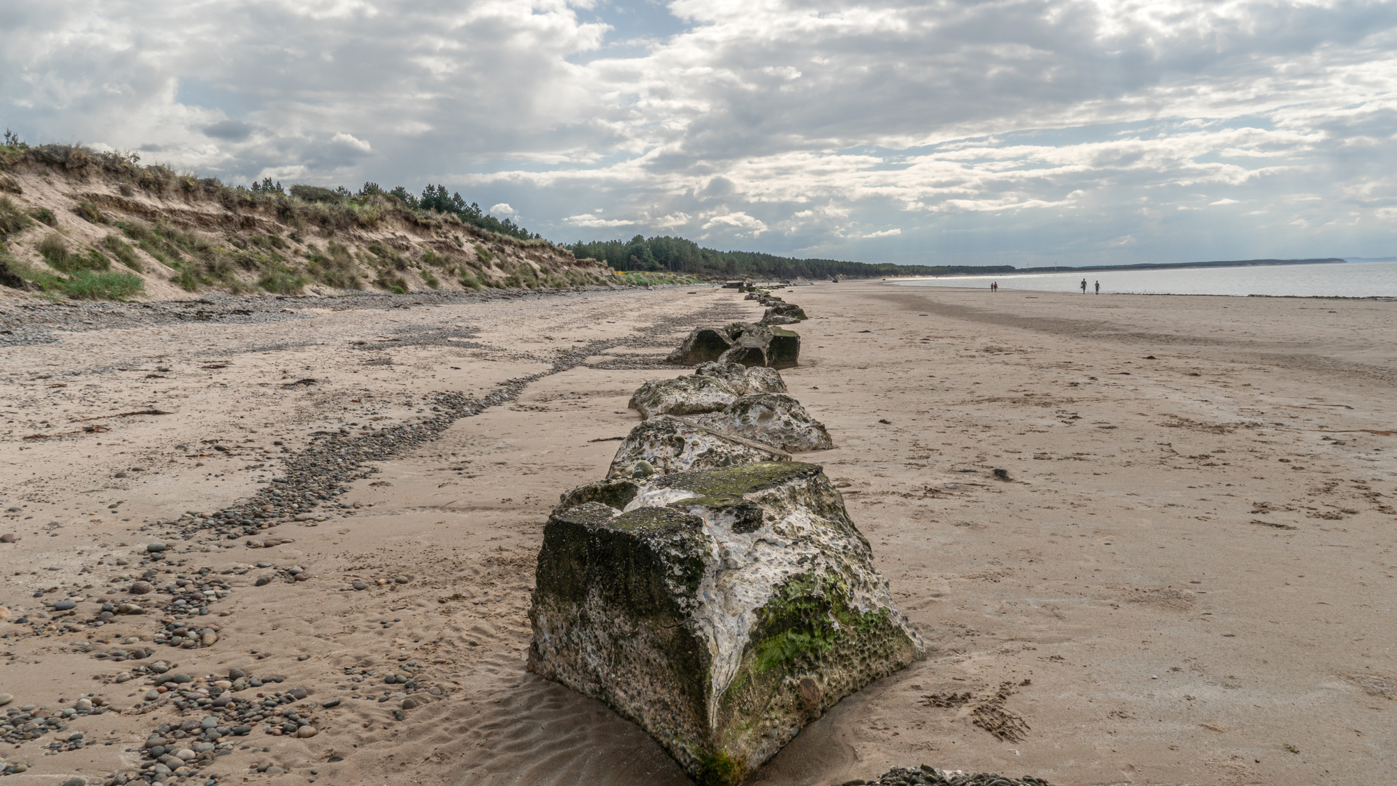 A row of tank barriers sit along a sand coastal beach