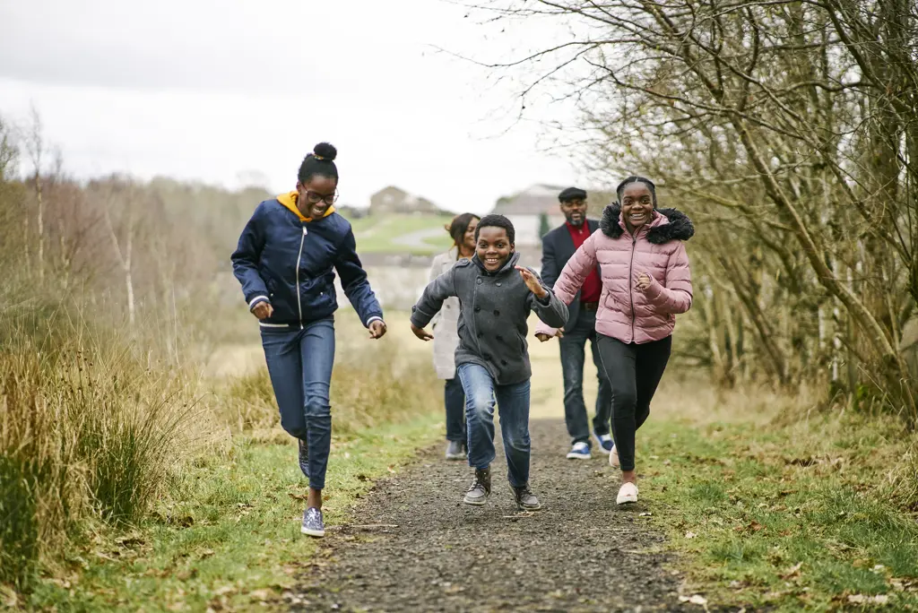 Children running along path at Cardowan Moss, Glasgow, with couple and housing estate in background.
