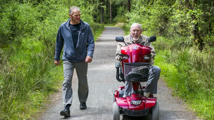 Person walking next to a person on a mobility scooter.