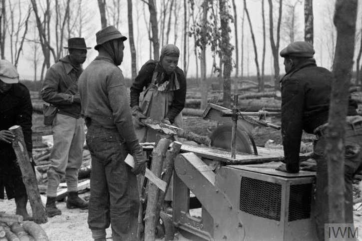 Black and white image of five foresters standing in an area of partially felled woodland using forestry machinery.