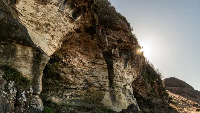 Caves with the sun appearing over the top of the cliff.