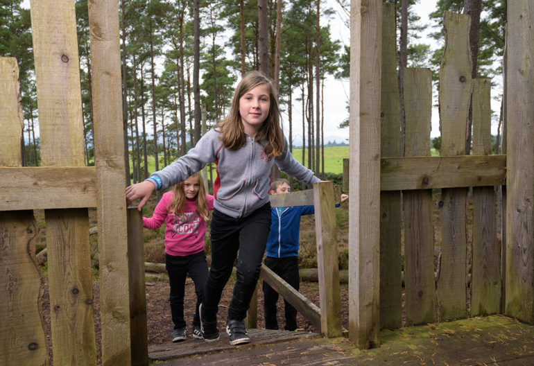 Two young girls and young boy playing in Natural Play Area, Camore Wood, Dornoch, Sutherland